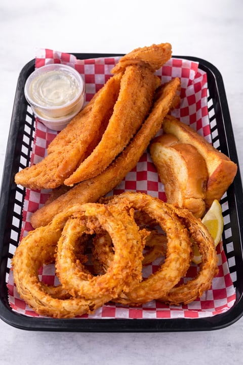 Black serving tray with red checkered paper containing fried calamari rings, fish and chips, and a white dipping sauce