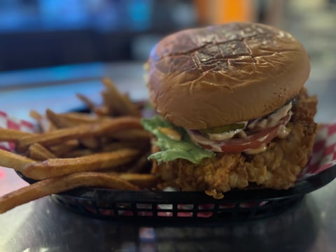 Fried chicken sandwich with lettuce and tomato on a toasted bun, served with french fries in a black basket