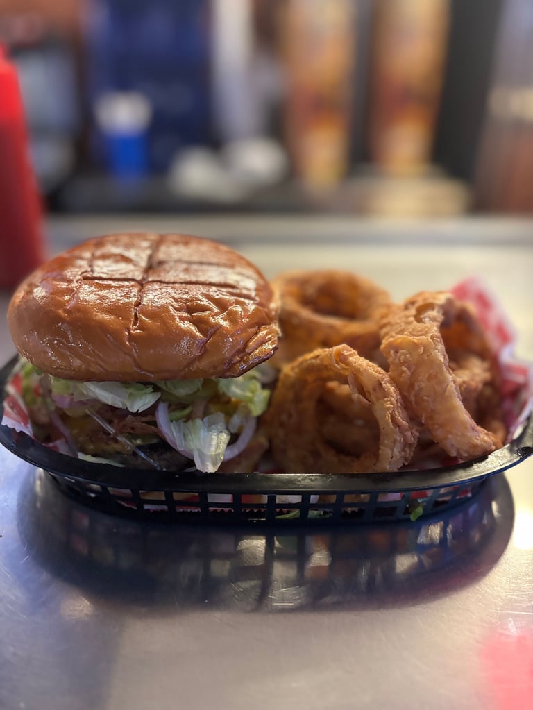Burger and onion rings served in a black paper basket on a table at a restaurant