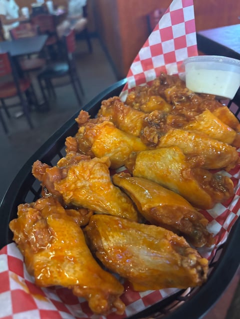 Crispy golden fried chicken wings served in a black container with red and white checkered paper in a casual restaurant setting