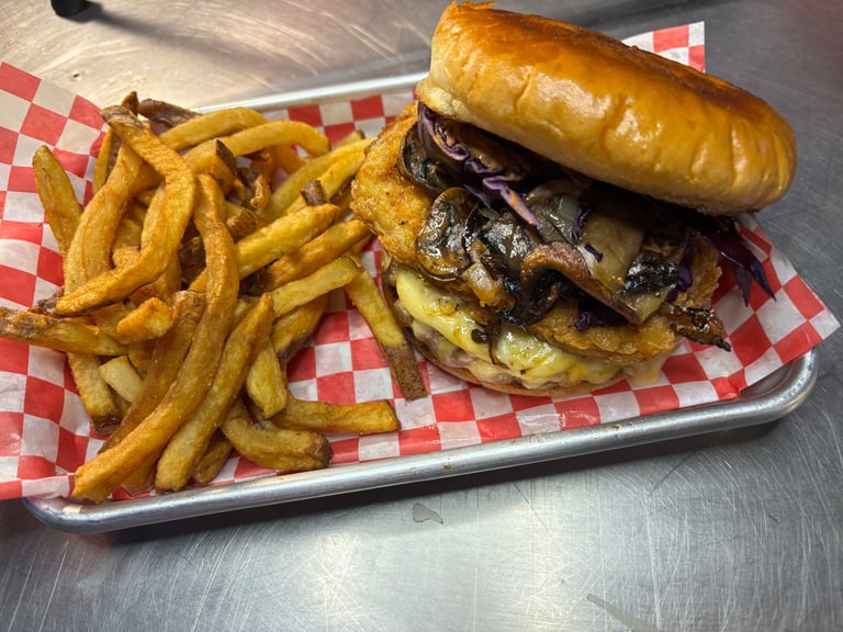 Gourmet burger with caramelized onions and cheese on a toasted bun, served with crispy french fries on a red checkered paper